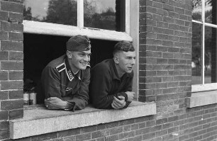 Zweiter Weltkrieg. Niederlande unter deutscher Besatzung. Zwei deutsche Wehrmachtsangehörige, aus einem Fenster schauend (wohl bei Den Haag)