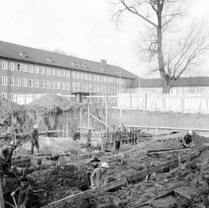Erweiterungsbau "Hochhaus" [später Gebäude B]: III. Bauabschnitt: im Vordergrund Baugrube mit Fundamenten an der Bangertstraße: darin Bauarbeiter: im Hintergrund Hauptgebäude [später Gebäude A] mit Erweiterungsbau II. Bauabschnitt