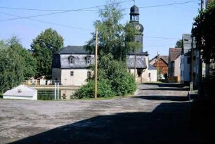 Dorfplatz mit Dorfteich, Entenhaus auf dem Wasser; hinten Kirche