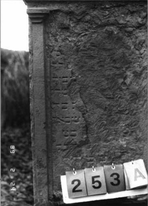 Grabstein 253 (Index: 99752173) Material: Sandstein Zustand: abgeblätt. mit fast völligem Textverlust Maße HxBxT: 128x59x15 cm Beschreibung: ädikulaart. Stele m. Pilastern, Giebel mit stilisiert. Eckakrot. , Schriftfeld eingeti Symbolik: Sternchen, Rundbogenfries: Grabstein 253A