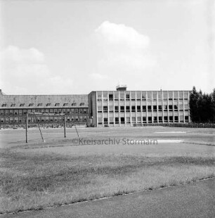 Sachsenwaldschule Gymnasium Reinbek: Schulstraße: Erweiterungsbau mit naturwissenschaftlichem Trakt: vorn Sportplatz: links Fußballtor: hinten rechts Fahrradständer mit Fahrrädern und Bäume hinter Jägerzaun: hinten links Altbau