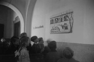 Dekorative Ausgestaltung der Klassenräume und Schulflure in der Einheitsschule Baumschulenweg und Oberschule Niederschöneweide in Vorbereitung des Deutschlandtreffens der Jugend für Frieden und Völkerfreundschaft zu Pfingsten 1950 : Schüler vor einem Plakat zum Deutschlandtreffen an einer Wand im Hausflur einer Schule
