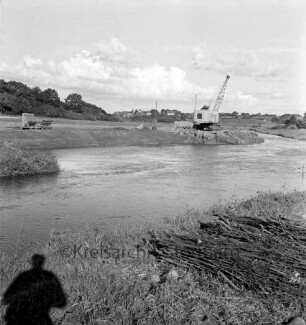 Trave: Flussregulierung: hinten links ausgebautes Teilstück, Lorenbahn: Bildmitte Bagger, abgestellte Loren: vorne Ufer, Reisigbündel, Schatten des Fotografen: hinten links Wiesen: hinten Häuser
