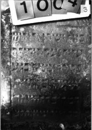 Grabstein 1004 (Index: 99751329) Material: Sandstein Zustand: verwitt/ein Akroter weggebrochen Maße HxBxT: 75x51x8 cm Beschreibung: eingezog. Rundbogenabschl. m. gekappten Pyramiden als Eckakroteren, Stele Symbolik: Blüte: Grabstein 1004B