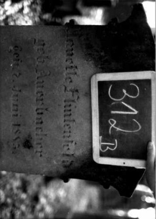 Grabstein 312 (Index: 100111992) Material: Sandstein Zustand: leicht verwittert Maße HxBxT: 110x55x25 cm Beschreibung: Stele, profilierter Sockel, giebelartiger Abschluß mit Verdachung, rechteckiges Schriftfeld eingetieft Symbolik: Kranz mit Schleife: Grabstein 312B