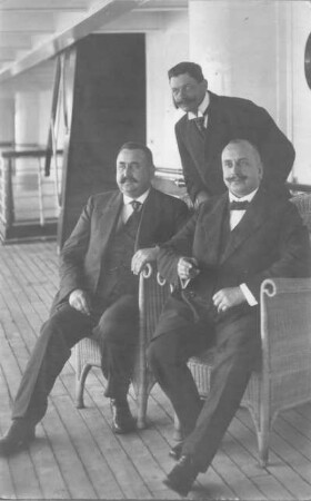 Kreuzfahrten der Hamburg-Amerika Linie, um 1911/1913. Drei Herren in Korbsesseln an Deck eines Hochseepassagierdampfers, vermutl. Pennsylvania (Druck; Weltpostkarte)