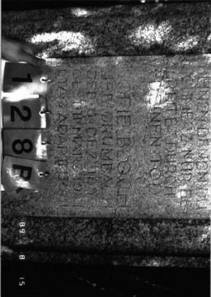 Grabstein 128 (Index: 100105327) Material: Granit Zustand: verwittert und gebrochen Maße HxBxT: 177x67x23 cm Beschreibung: Stele, Rundbogenabschluß nach unten in Voluten auslaufend, erhabenes Schriftfeld Symbolik: Voluten, Blattwerk über Schriftfeld: Grabstein 128B