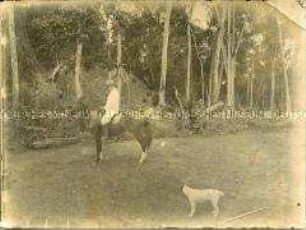 Der Stationsleiter von Molundu auf einem Pferd mit einem Hund im Vordergrund