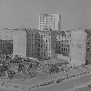 Berlin. Fläche mit Trümmerschutt und Gebäuderesten gegen mehrstöckige Wohnhäuser und Hochhaus