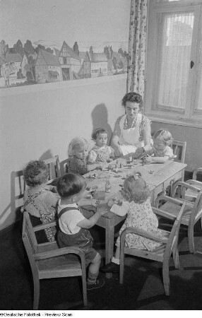 Kleinkinder an einem Tisch spielen unter Aufsicht einer Erwachsenen Person mit Holzspielzeug