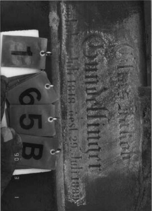 Grabstein 165 (Index: 100114998) Material: Sandstein und ? Zustand: beschädigt, Text sehr gut Maße HxBxT: 230x68x32 cm Beschreibung: Stele auf gestuftem Sockel, Spitzgiebel mit Eckakroteren, Texttafel mit Rundbogen: Grabstein 165B