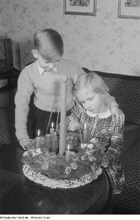 Zwei Kinder beim Entzünden der Kerzen eines Adventskranzes