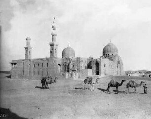 Kairo, Ägypten. Blick auf ruinöse Anlage mit Kuppeln und Minaretten (Mameluckengräber?), im Vordergrund Kamelkarawane mit Einheimischen