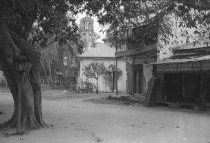 Dorfplatz : Platz vor einem großem Gebäude; in der Mitte ein Baum.