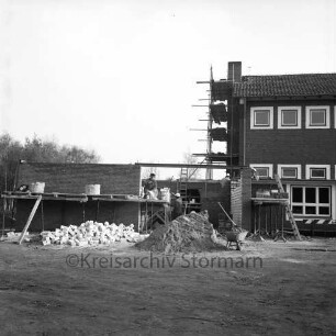 Schule Am Reesenbüttel: Volksschule: Schimmelmannstraße: Verbindungstrakt zur Turnhalle in Bau: Maurer beim Aufmauern der Wände: Arbeitsplattform, Leitern, Blechtonnen: davor Sandhaufen, Haufen mit Mauersteinen, Schubkarre: an Giebel von Klassentrakt Gerüst