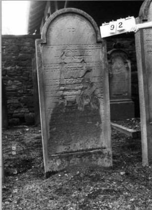 Grabstein 92 (Index: 100094796) Material: Sandstein Zustand: verwittert, abgeblättert, Textverlust Maße HxBxT: 170x70x12 cm Beschreibung: Stele, eingezogener Rundbogenabschluß: Grabstein 92