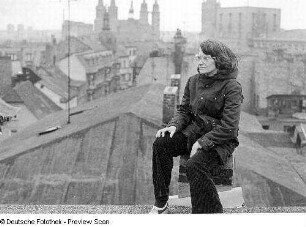 Halle (Saale). Blick vom Dach eines Hauses über die Innenstadt. Junge Frau auf einer Esse sitzend