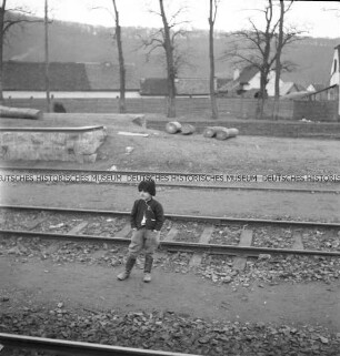 Ein an Bahngleisen stehender ungarischer (?) Junge mit Pelzmütze