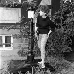 Ferien vom Ich. Frau, neben einer Handschwengelpumpe stehend