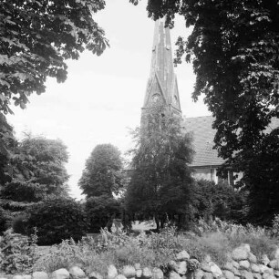 Friedenskirche: Außenansicht von Süden: vorn Feldsteinwall mit Bewuchs: dahinter Kirchhof: rechts und links Bäume