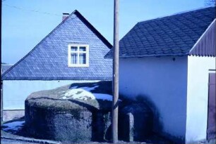 geschlossener Brunnen aus massivem Gestein, davor renoviertes Brunnenhaus