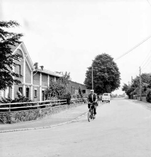 Dorfring: links Bauerngehöft mit Mauer und Zaun: vorn Fahrradfahrer: hinten rechts VW-Bus: dahinter Bäume