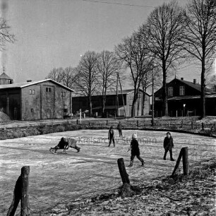 Dorfteich mit Schlittschuhläufern: dahinter Heilsaustraße: im Hintergrund Bauernhäuser und Bäume: Winter