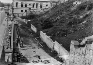 Mauerreste : Mauerreste an einem Hang. Davor ein Bürgersteig mit Passanten und eine weitere Mauer.