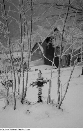 Schneelandschaft mit Kreuz, im Hintergrund Wohnhäuser