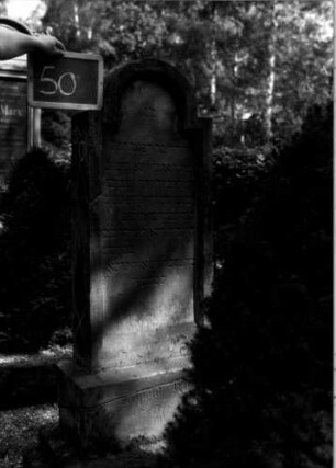 Grabstein 50 (Index: 100109994) Material: Sandstein Zustand: im Sockel gebrochen, verwittert Maße HxBxT: 130x47x17 cm Beschreibung: Stele, getreppter Sockel, eingezogener Rundbogenabschluß mit Verdachung, Schriftfeld eingetieft Besonderheit: auf Rückseite eingravierte Nr.: 93: Grabstein 50