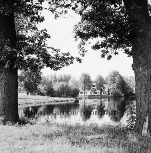 Mühlenteich: hinten rechts Mühlengebäude: links hinter Bäumen weitere Gebäude: vorn rechts und links Bäume