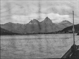 Stadt am See : Blick von einem Schiff auf eine Stadt an einem See, im Hintergrund Gebirgszüge