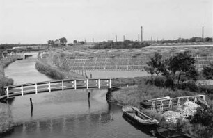Glashauslandschaft-Westerland : Blick über eine Landschaft mit einem kleinen Kanal, Brücke, Booten und Gewächshäusern