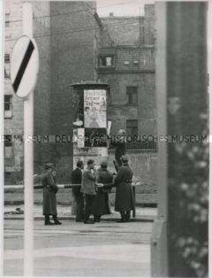 Anbringung eines Plakats (zu Flucht oder Fluchtversuch?) an Litfassäule in Berlin-Ost (von Westen gesehen)