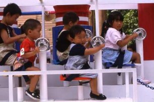 Tokio. In einem Vergnügungspark sitzen Kleinkinder auf einem Karussell