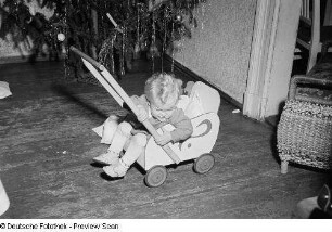 Porträt eines kleinen Mädchens mit Puppenwagen vor einem Weihnachtsbaum