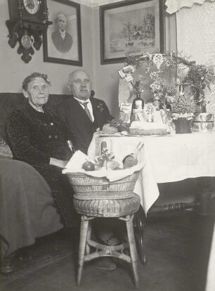 Goldenes Hochzeitspaar, am Gabentisch im Wohnzimmer sitzend