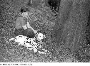 Die Bildhauerin Thea Richter mit einem Dalmatiner in einem Wald (?),neben einem Baum sitzend