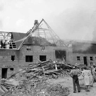 Brand: Bauernhof von Paul Haase: brennendes Wohn- und Wirtschaftsgebäude: davor Dachsparren: links im Dachstuhl Feuerwehrmänner beim Löschen: im Vordergrund rechts Bewohner des Hauses