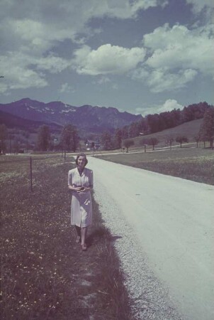 Deutschland. Junge Frau an einer Landstraße vor einer Bergkette (vielleicht in Bayern)
