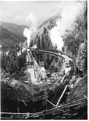 Rückbau des Ravennatunnels, alter Viadukt mit einem darauf befindlichem Eisenbahnzug und Fahrbahnarbeiten am neuen Viadukt