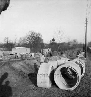 Abwasser: Papenwisch / Wöhrendamm: Bau der Kanalisation: vorn rechts Betonröhren: dahinter Arbeiter an Bauschacht: hinten links Baumaterial, Lieferwagen und Baubude: rechts Strommasten: dahinter Häuser mit Gärten