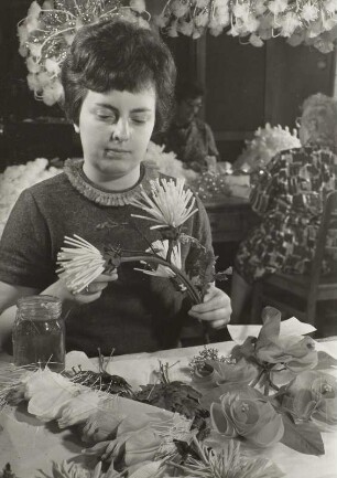 Blumennmacherin Renate Hantsch von der PGH Einheit, spätere Kunstblume Sebnitz, bei der Endfertigung textiler Distelblüten. Im Vordergrund Tulpenblätter und Phantasie-Rosen
