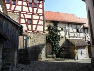 Kirchhof im Nordwesten von Süden mit Gaden (Kirchhofmauer mit Wehrgang als Außenmauer - Gaden mit Fachwerkobergeschoß sowie vorgebauten Kellereingängen)