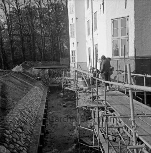 Restaurierung: innerer Graben: neue Grabenversteifung mit Holzbohlen am Grabenfuß: Grabenböschung nach Wiederherstellung mit alten Findlingen: Arbeiter auf Gerüst an Fundament