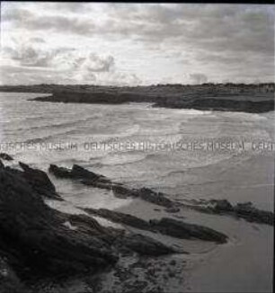 Strand in einer Bucht mit Felsen an der französischen Atlantikküste, im Hintergrund Häuser