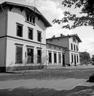 Bahnhofsgebäude: Straßenfront: davor Straßenlampen, Briefkasten, Verkehrsschild, angelehntes Fahrrad: vorne Bahnhofstraße, Bürgersteig