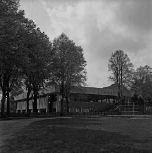 Stormarnhalle: Bürgerpark: vorn Grünfläche mit Bäumen: dahinter Weg und Jägerzaun: hinten rechts Spielplatz mit Klettergerüst