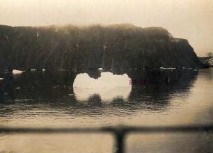 Spitzbergen. Schwimmender Eisberg gegen Felsenküste und Buchtlandschaft über die Reeling des Hochseepassagierdampfers "Victoria Luise"