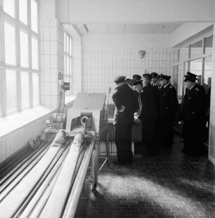 Kreisschlauchpflegerei (Kreisfeuerwehrzentrale) Stormarn: Nütschau: Einweihung: Feuerwehrleute besichtigen die Schlauchwaschmaschine, vorne links ein Tisch auf dem Schläuche abgedrückt und auf Dichtigkeit überprüft werden